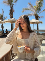 Woman holding a cup of coffee outdoors with palm trees and a clear sky in the background