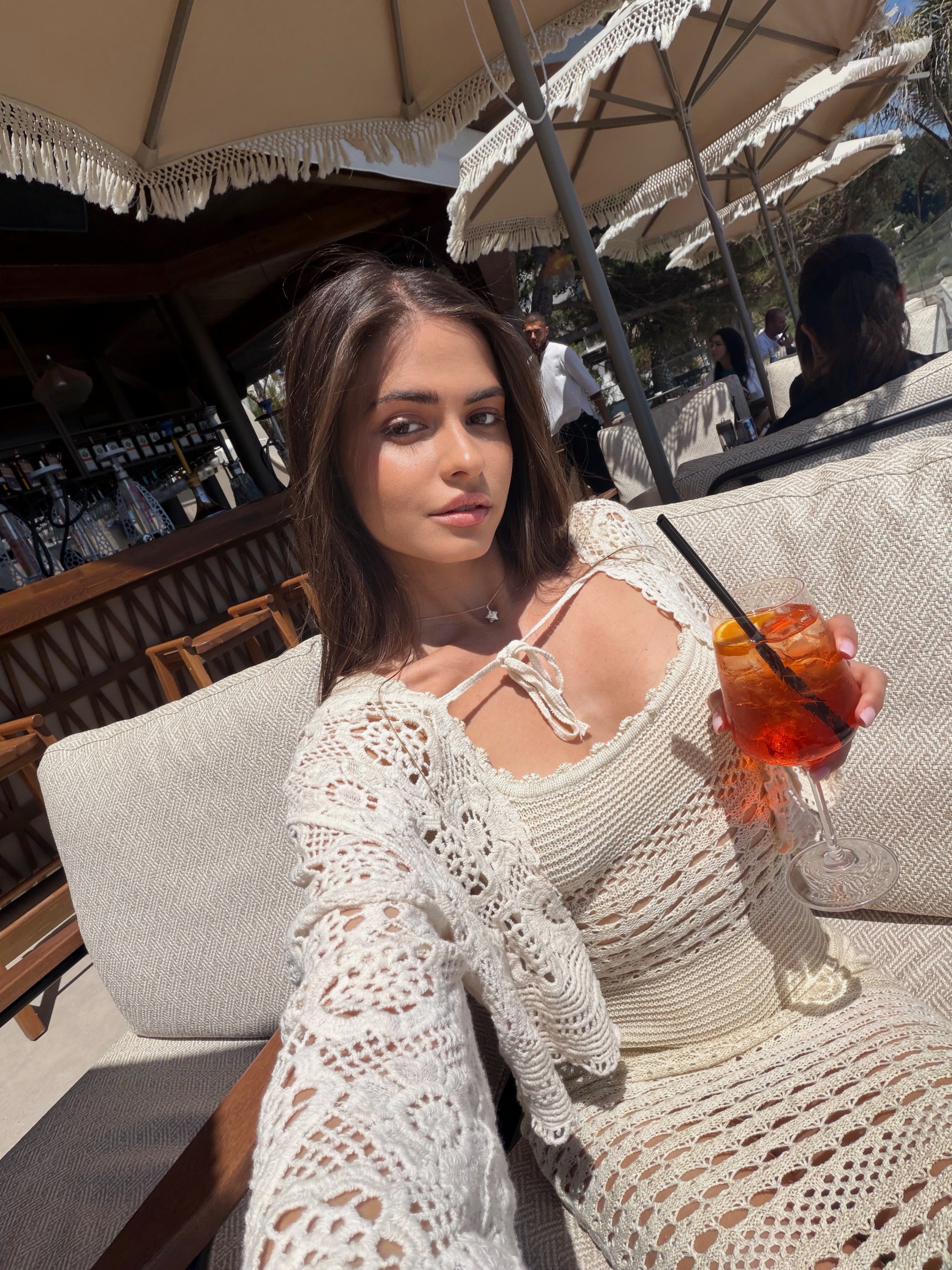 Woman in a white lace dress holding a drink outdoors