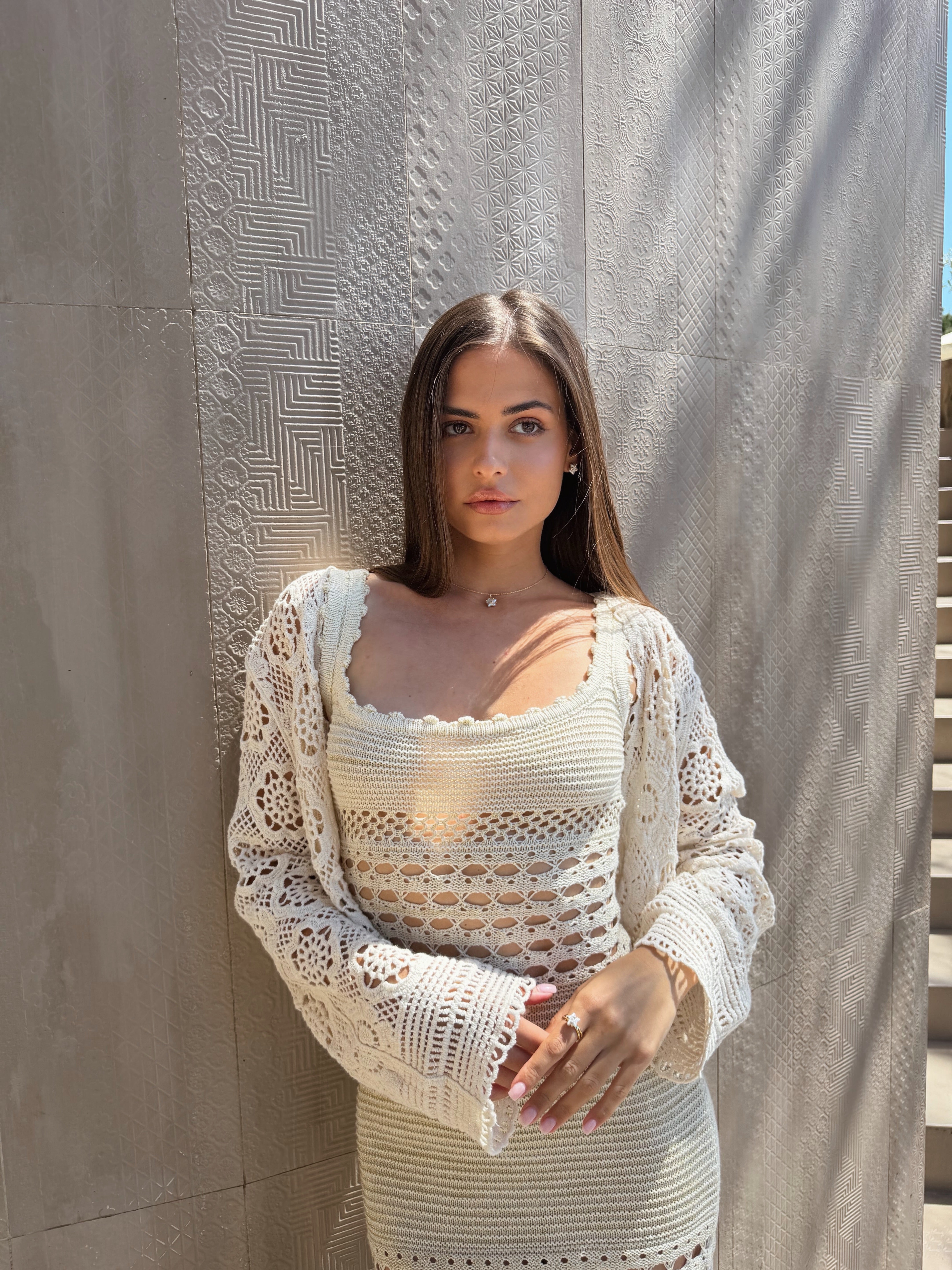 Woman wearing a white crochet dress standing against a textured wall.